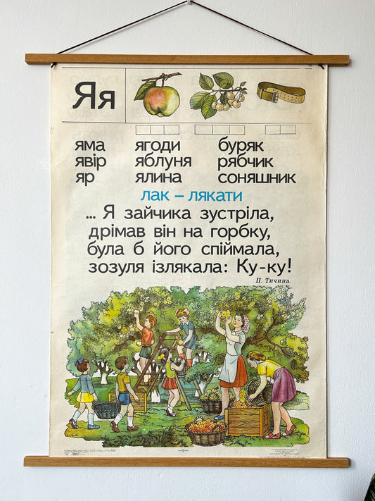 A Ukrainian vintage children's alphabet nursery poster printed in 1983 with an illustration of a family apple harvest scene and educational text to teach the Ukrainian language to children.