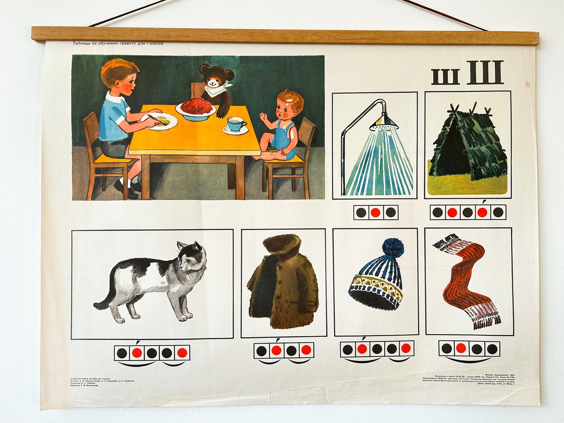 An original Soviet vintage phonetic Russian alphabet poster printed in Moscow in 1978, with colourful illustrations of a cat, a boy eating with a doll and a teddy bear, a shower, a hat, a scarf, a fur coat and a hut.