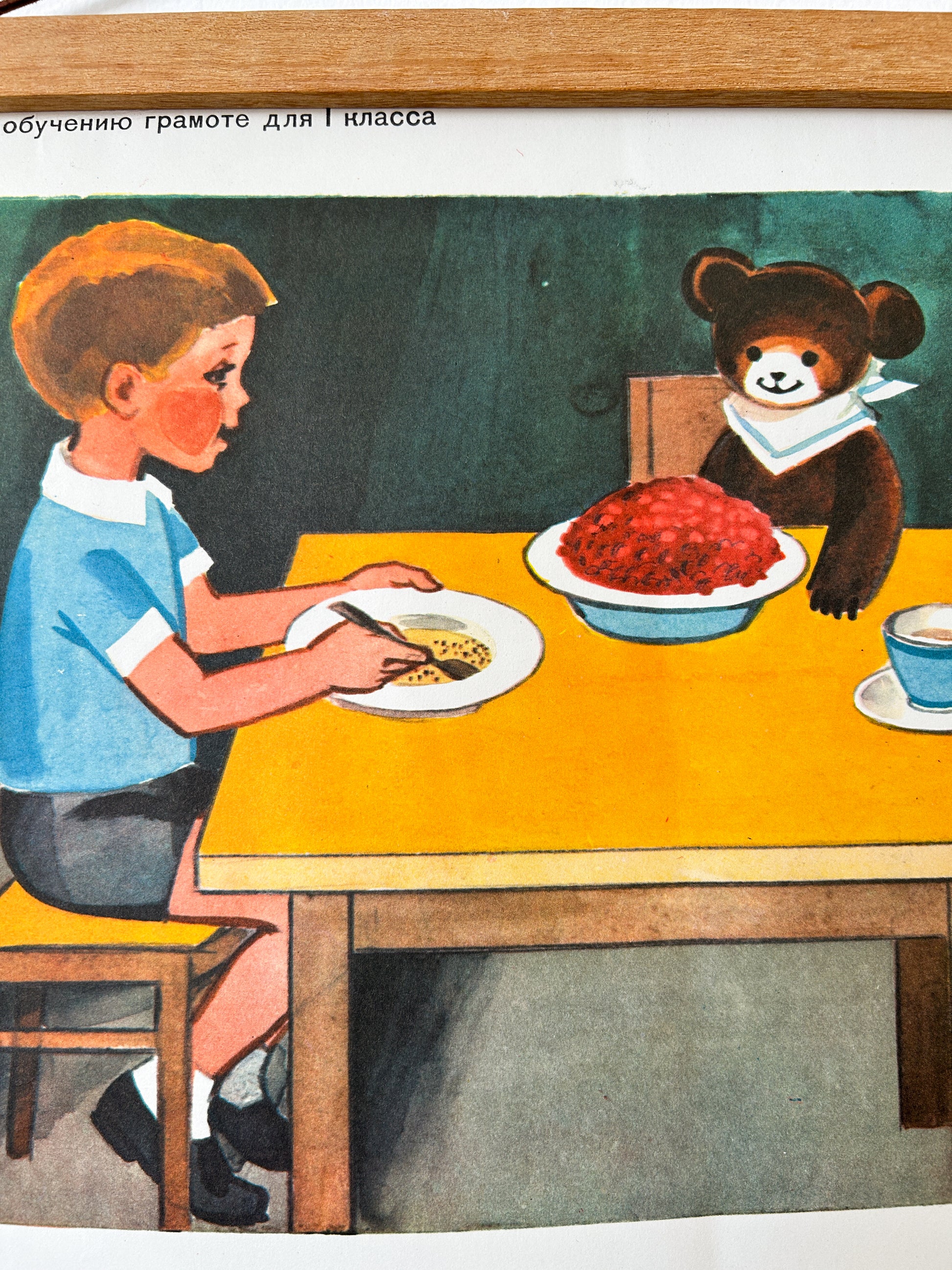 USSR vintage children's poster detail – an illustration showing a boy at a table eating with a spoon while a teddy bear sits across from him with a bowl of red food. 