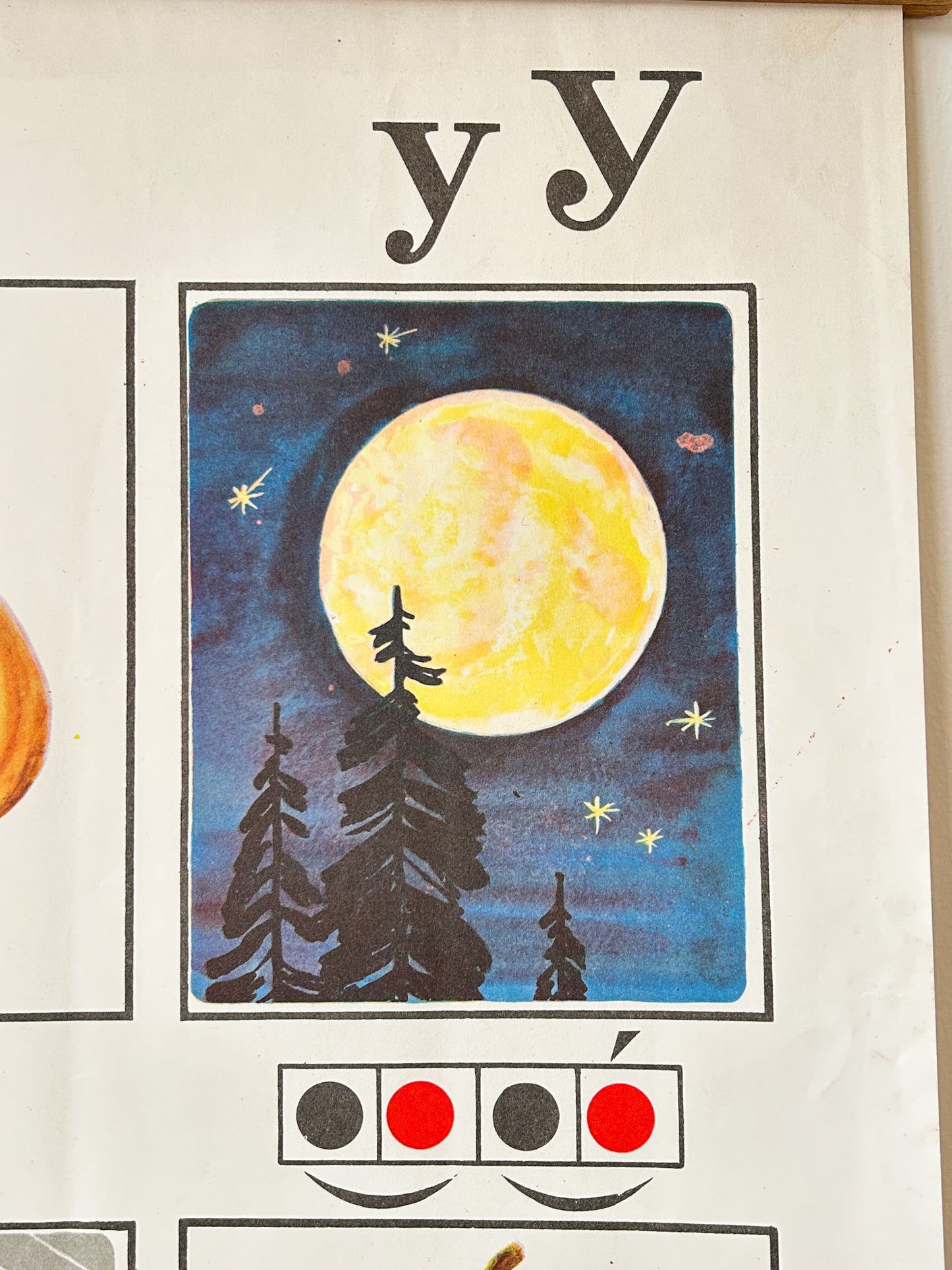 A close-up of a USSR vintage educational poster or chart showing the letter 'y' with a colourful illustration of a moonlit night scene featuring a large yellow moon, dark blue sky, and black tree silhouettes. A phonetic diagram of the word moon below the illustration.