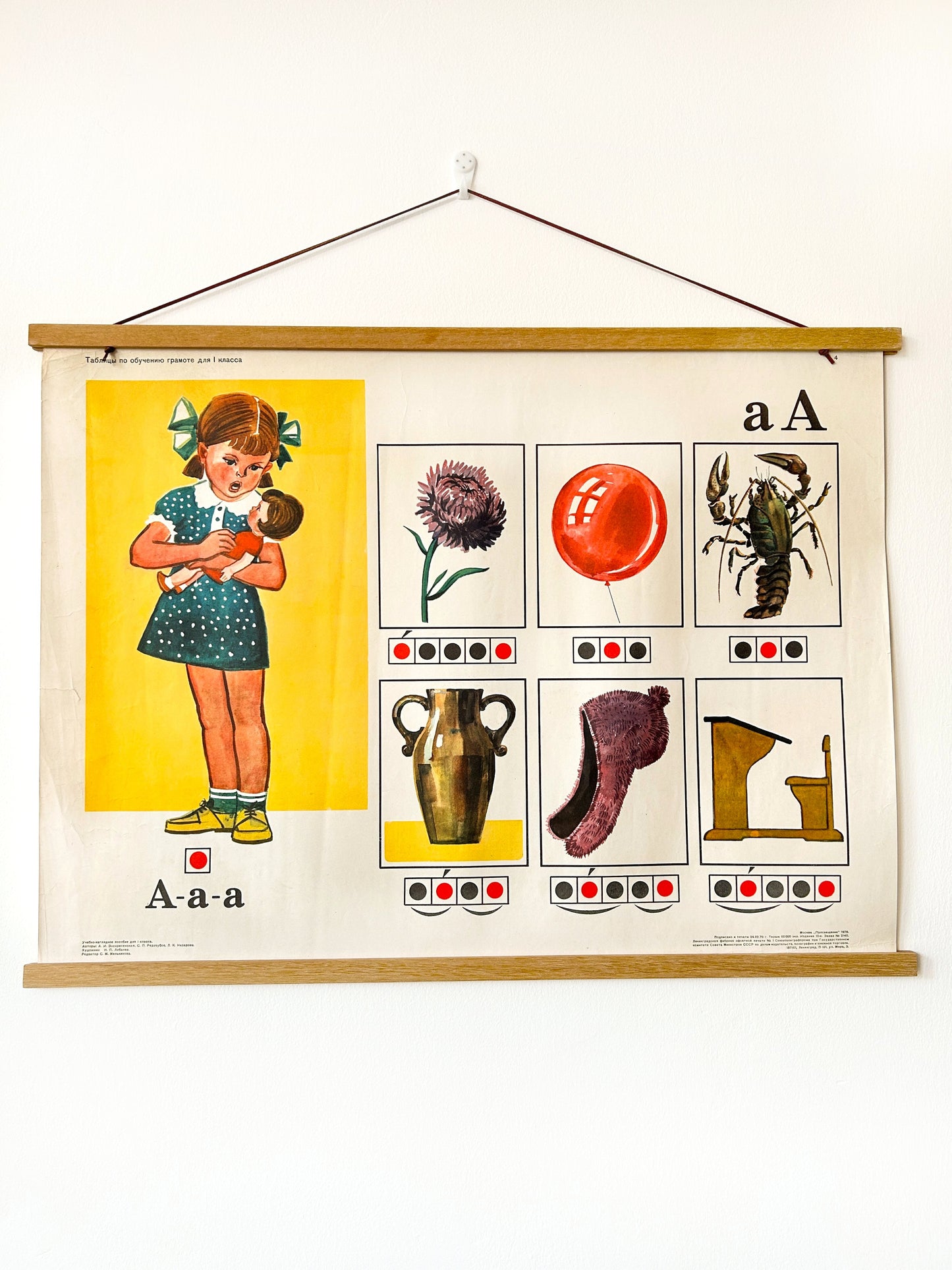 An original Soviet vintage colourful phonetic Russian alphabet poster for a letter A printed in Moscow in 1978, featuring a girl with a doll, a balloon, a flower, a hat, vase, crayfish and a school desk. 