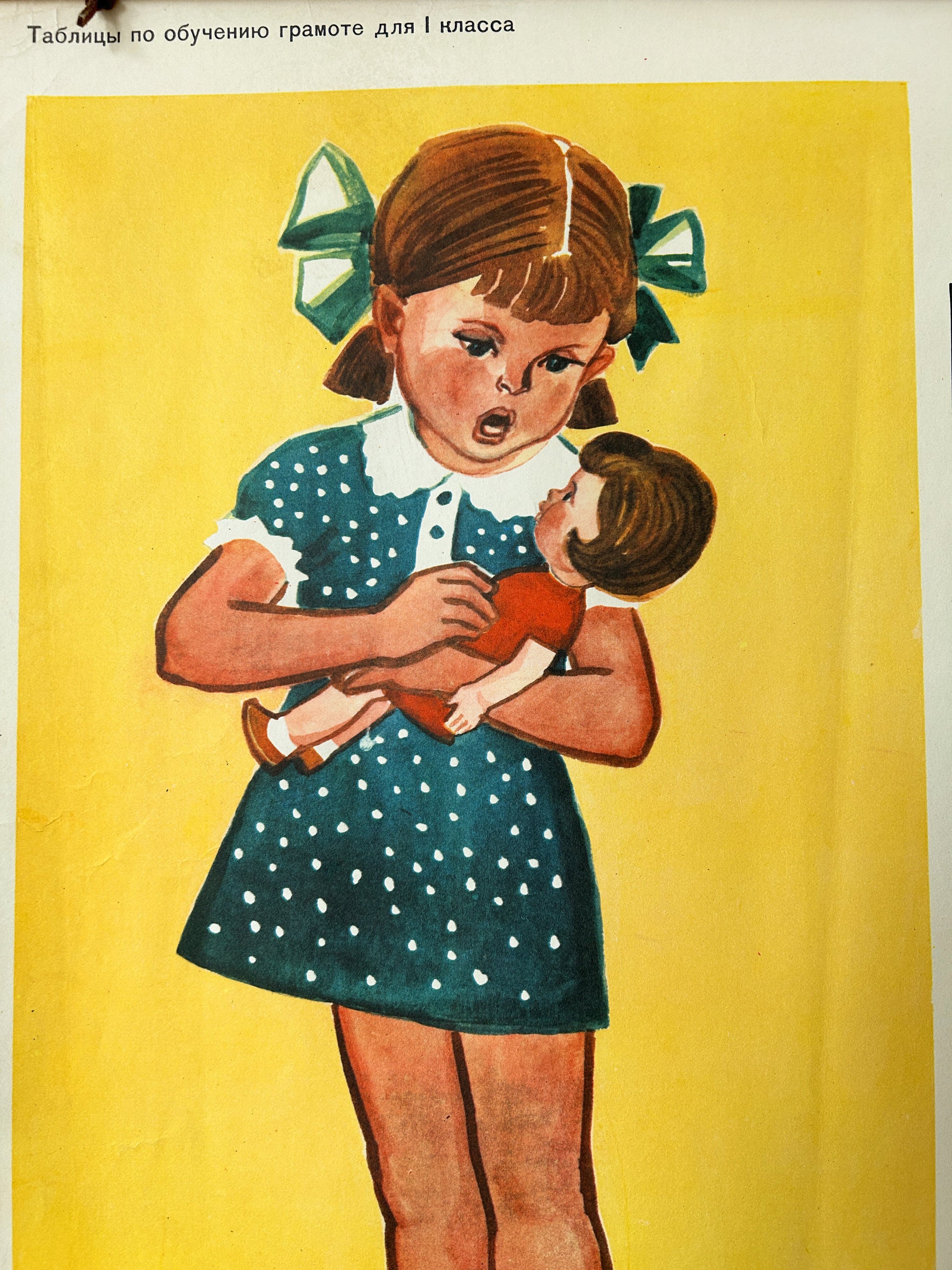 USSR vintage educational alphabet poster detail featuring illustration of a young girl with brown hair in a green bow holding a doll, set against a solid yellow background with Russian text at the top.