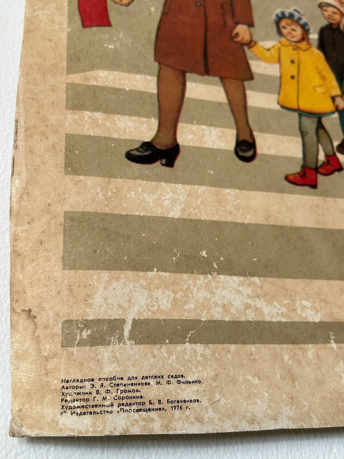USSR vintage road safety poster detail: a crosswalk scene with part of a woman in a brown coat and black shoes, a child in a yellow coat, and another child in a blue hat and red shoes, printed on aged tan paper with small Cyrillic text at the bottom.