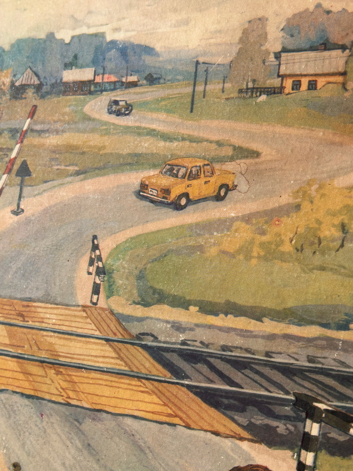 USSR vintage road safety poster detail:  scene of a winding country road with a yellow car, houses, trees, and a railway crossing in the foreground.