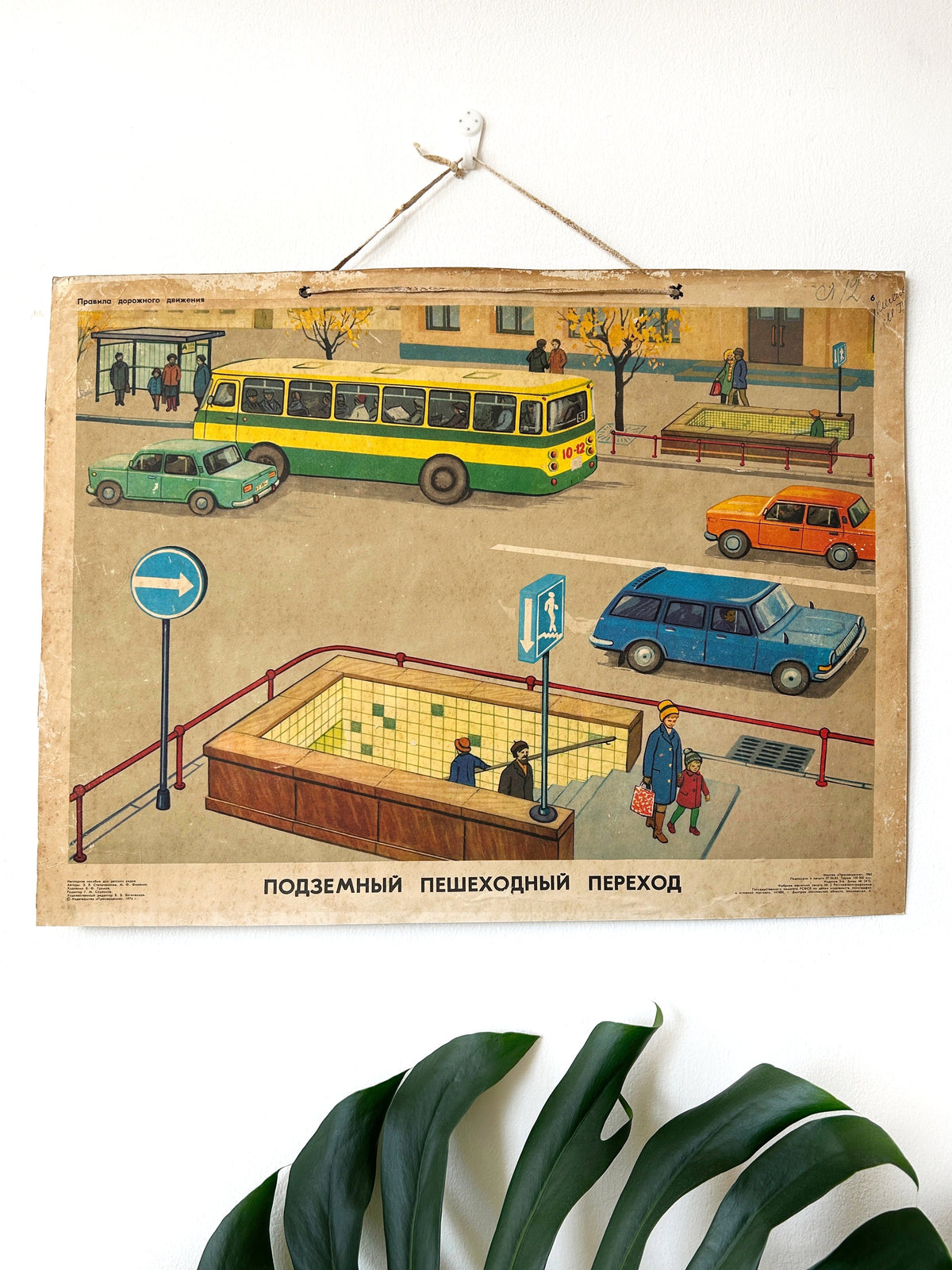 USSR vintage illustrated nursery road safety poster showing a street scene with pedestrians using an underground crossing, a yellow and green bus, cars and Russian text at the bottom.
