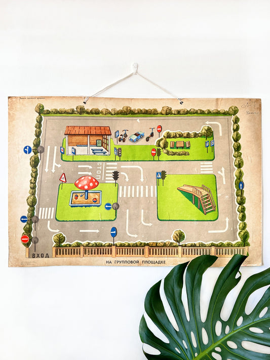 A large USSR vintage chart used in kindergartens and schools to teach children road safety, traffic signs, and pedestrian etiquette, hanging on a white wall with monsterra leaf below.