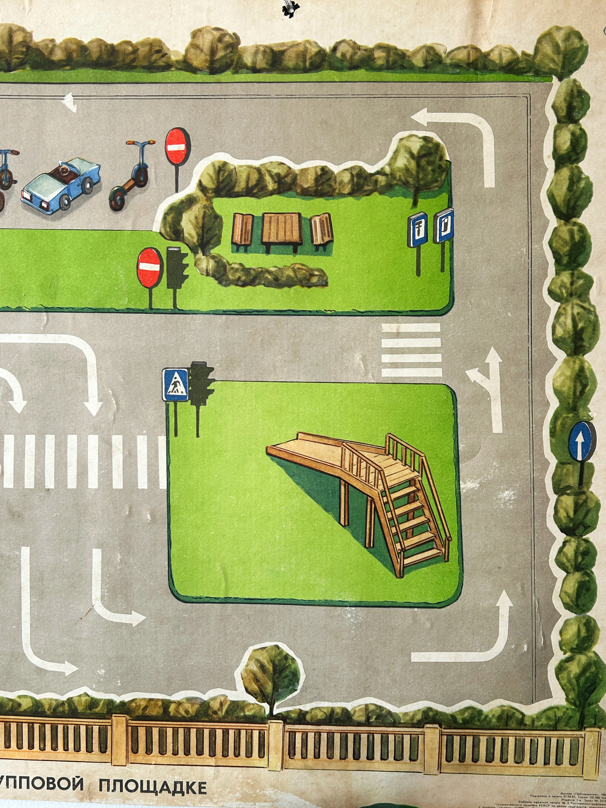 A close-up of a colourful USSR vintage children's road safety poster showing a street scene with a grey road, a playground with a slide, crosswalks, traffic lights, green grass areas, benches, a bus stop, parked scooters and a car.