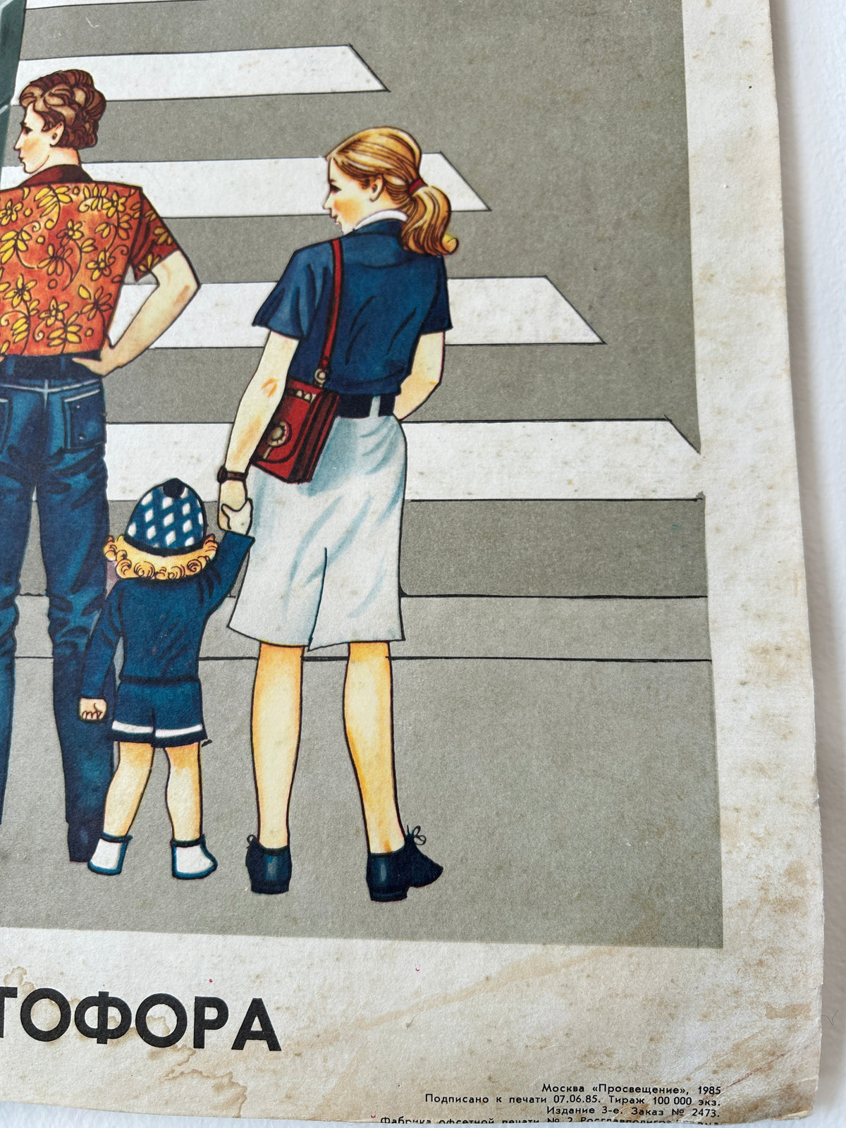 Close-up corner detail of a vintage USSR road safety poster showing a family of three: a father, mother and a toddler at a crosswalk, with Russian text with details about the printers at the bottom. 