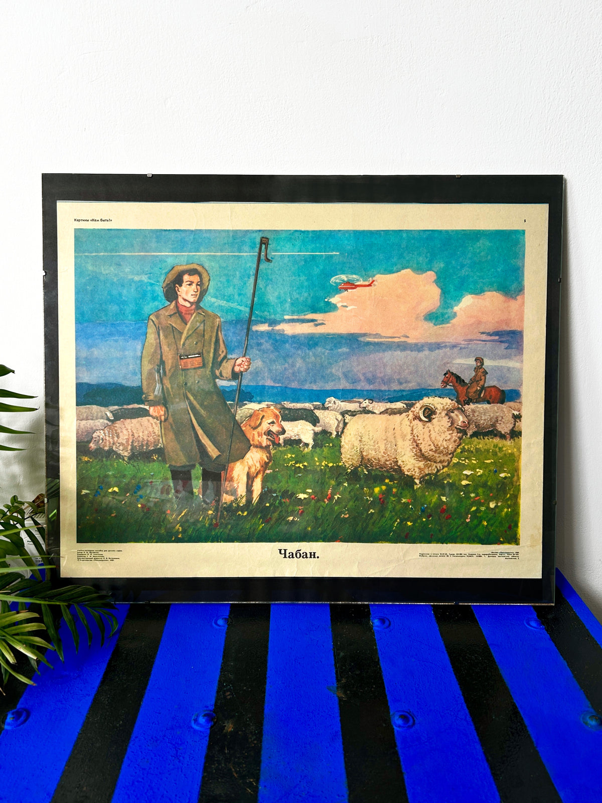 A framed Soviet vintage art print depicting a shepherd with a dog and sheep under a blue sunset sky, with a helicopter flying above and a horse in the background.
